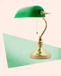 Green desk lamp with a brass base and pull chain, set against a pastel background.
