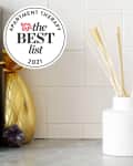 White reed diffuser, gold pineapple decor, and succulent on a wooden tray against a tiled wall.