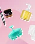 Hair styling tool, skincare pump bottle, makeup organizer, scalp massager, and white towels on a pink background.