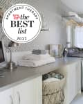 Laundry room with patterned wallpaper, washer, dryer, ironing board, and a basket of towels on a countertop.