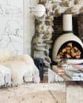 Living room with painted white slat ceiling and walls, white shag rug, white accent chair with tasseled throw, white freestanding fireplace surrounded by rock