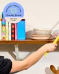 Cleaning Awards Specialty Tools seal on a photo of someone dusting the top of their kitchen shelf's microwave