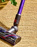 Dyson vacuum cleaner attachment on a woven rug beside a wooden table with books and a potted plant.
