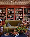 Cozy living room with green sofa, floral wallpaper, bookshelves, and a vase of tulips on a blue table.