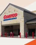 Costco Wholesale storefront with stone facade, red bollards, and shopping carts near entrance.