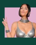 Woman in metallic silver top and jewelry, making peace signs with both hands against a pink and green background.