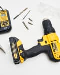 Yellow and black DeWalt drill with charger, Stanley hammer, drill bits, screws, and spackling paste on a white surface.