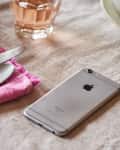 iPhone on a linen tablecloth beside a pink napkin, spoon, knife, and glass of rosé.