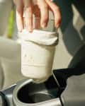 Hand placing a glass wrapped in a white sock into a car cup holder.