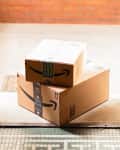 Two Amazon packages stacked at an open doorway on a tiled floor.