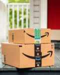 Two Amazon packages on a porch with a red door and white railing.