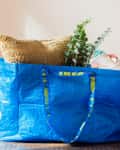 Blue IKEA bag on a table filled with a burlap pillow, eucalyptus branches, and folded textiles.