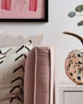 Speckled pumpkin on a white table with a vase of flowers, candle, and decorative skull under a glass dome.