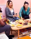 Four friends playing cards around a coffee table with snacks, drinks, and a large jar of cheese balls in a cozy living room.