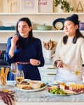 Three people enjoying wine and snacks in a modern kitchen with marble countertop and open shelves.