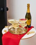 Champagne glasses on a gold tray with a bottle of prosecco on a red cloth with gold stars.