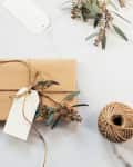 Gift wrapped in brown paper with twine, eucalyptus sprigs, scissors, and a blank tag on a marble surface.