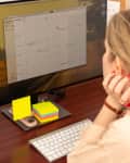 A woman sitting at a computer desk, reviewing a digital calendar app