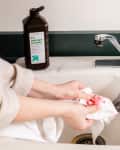 Person washing a stained white cloth in a sink with hydrogen peroxide bottle nearby.
