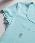 Light blue t-shirt with small green stains on the front, lying on a marble surface.