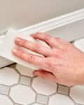 person using magic eraser on white baseboards
