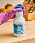 Person wearing pink gloves holding a bleach bottle on a kitchen counter.