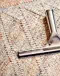Metal carpet rake on a textured beige and orange patterned rug.