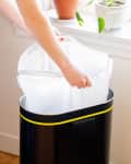 someone putting a white trash bag into. trash can