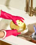 angled shot of someone hand washing a dish with a yellow scrub daddy