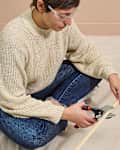 A person sitting on a canvas dropcloth cutting wood trim with miter shears