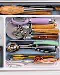 Kitchen drawer filled with various utensils including wooden spoons, a timer, measuring cups, and a whisk.