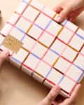 Two hands holding a gift wrapped in patterned paper with a tag, surrounded by other wrapped presents.