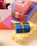 Colorful wrapped gifts in various patterns, including a pink bag with a tag, arranged on a light surface.