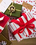 Colorful wrapped gifts with ribbons and tags on a wooden surface, featuring festive patterns and a mistletoe decoration.