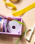 Crafting supplies on a table, including scissors, colorful ribbons, and patterned wrapping paper rolls.