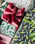 Colorful wrapped gifts with various ribbons, including green, pink, and red, on a patterned background.