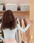 Woman organizing a closet with hanging shelves, folded clothes, and storage bins.