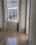 Empty room with light wood flooring, a large window with gray trim, and a baseboard heater.