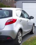Silver car parked in front of a closed white garage door on a paved driveway.