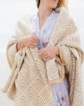 Woman wrapped in a beige geometric patterned blanket on a beach, wearing a floral dress.