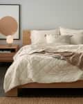 Cozy bedroom with a wooden bed, cream bedding, two bedside tables with lamps, and abstract wall art.