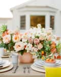 Outdoor dining table with floral centerpiece, candles, and place settings featuring citrus fruits and yellow napkins.