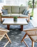 Patio with wicker chairs, gray sofa, striped cushions, concrete table, and potted plants on a patterned rug.