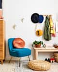 Mid-century modern room with a wooden dresser, blue chair, wall hooks with hats, and a woven basket on the floor.