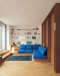 Modern living room with blue sectional sofa, wooden floors, built-in shelves, and large windows.
