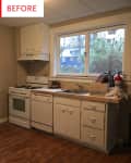 Small kitchen with white cabinets, gas stove, dishwasher, and large window overlooking trees.