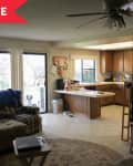 Living room with sectional sofa, striped armchair, large TV, and open kitchen with wooden cabinets and island.