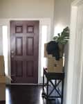 Entryway with maroon door, moving boxes, and a small table with a plant and black cloth.
