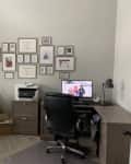 Home office with a gallery wall, desk, computer, printer, and stacked chairs. Red "Before" label in the corner.