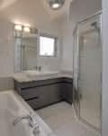 Bathroom with a large bathtub, glass shower, dark vanity, and open shelving.